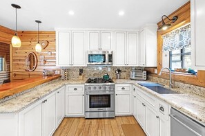 A modern kitchen with white cabinets, a stainless steel stove, a microwave, and a sink.