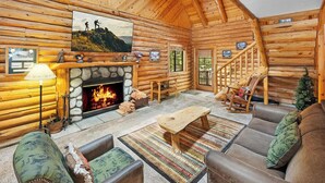 A log cabin interior with a fireplace, wooden walls, a staircase, and a cozy seating area.