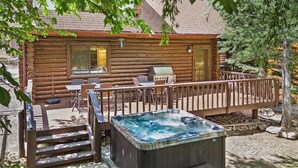 A log cabin with a hot tub, outdoor seating, and a grill.