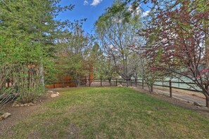 A fenced backyard with a grassy area, trees, and a wooden fence. - Bear Mountain Log Lodge By Destination Big Bear: Walking distance to Bear Mountain,Golf Course and Hiking Trails! Hot Tub! Fenced Yard! Pet Friendly! (Big Bear Lake)
