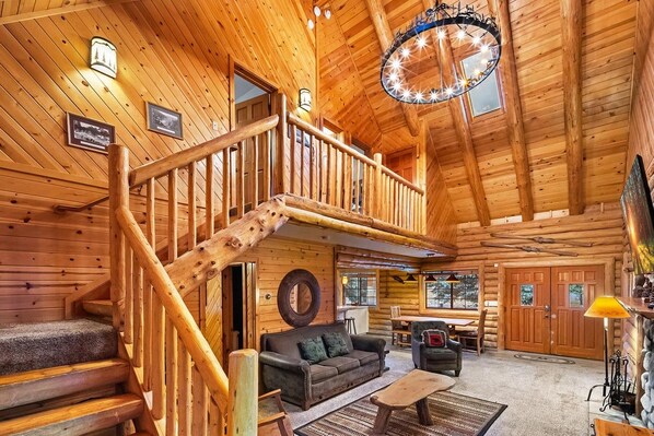 A log cabin interior with a staircase, a living room with a sofa and coffee table, and a dining area.