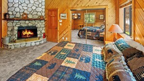 A cozy log cabin interior with a stone fireplace, a quilted bedspread, and a wooden ceiling.