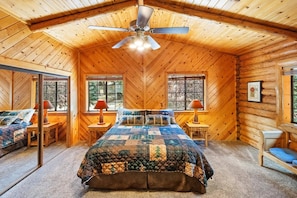 A log cabin bedroom with a large bed, two bedside tables, a ceiling fan, and windows.
