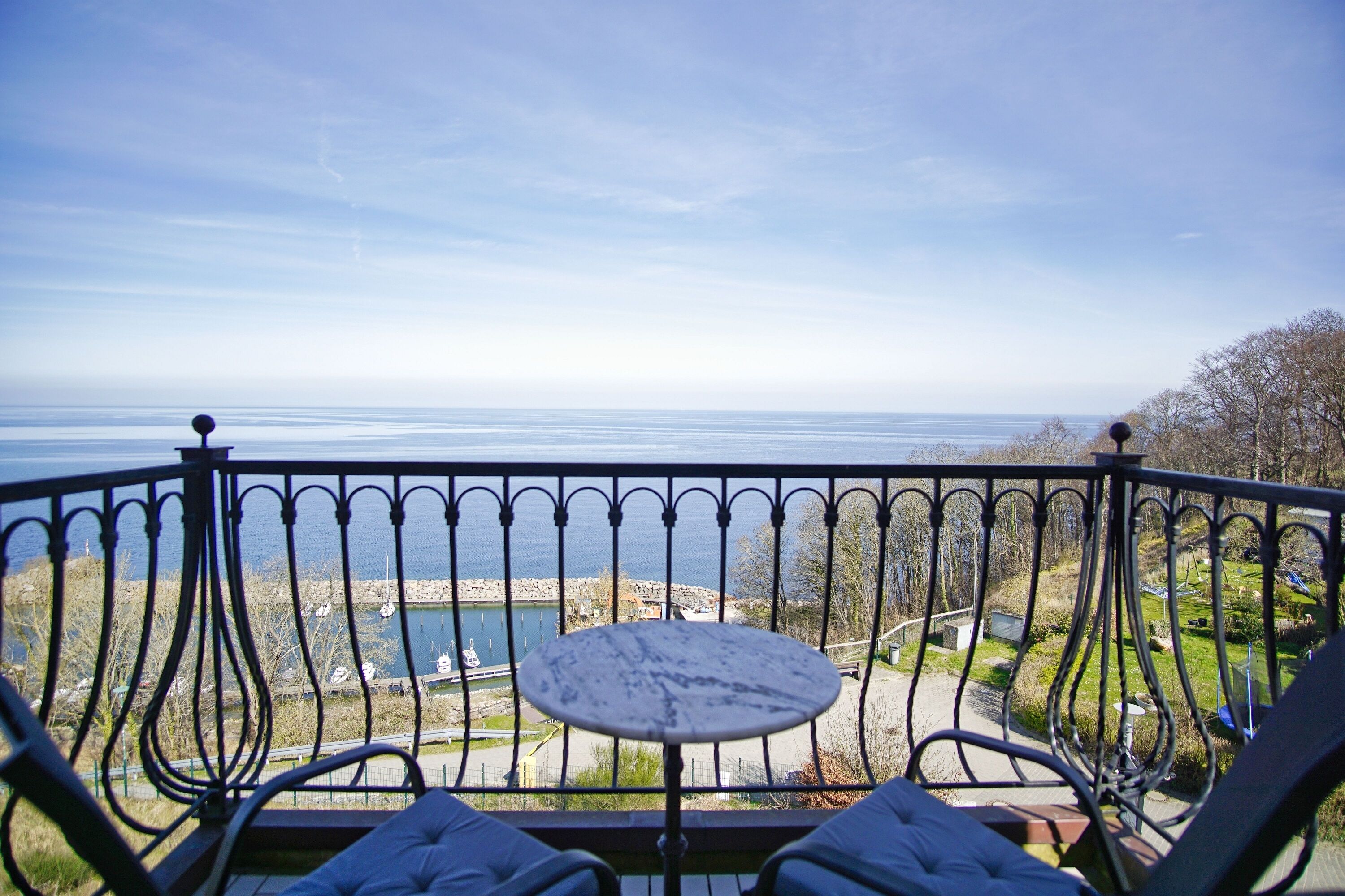 Ein Balkon mit rundem Tisch und zwei Stühlen mit Blick auf ein Gewässer und einen Park.