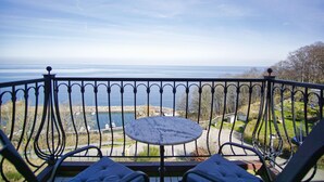 Un balcón con una mesa redonda y dos sillas, con vista a un cuerpo de agua y un parque.