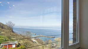 Vista costera desde una ventana con vista al mar tranquilo, cielo despejado y tierra a lo lejos.