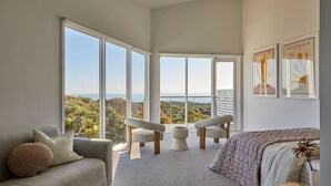 A spacious bedroom with large windows offering a view of the landscape. There are two chairs and a bed with a view. - The Cape Retreat with stunning views (Cape Schanck)