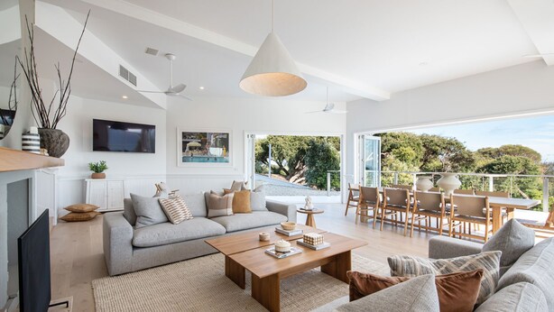 A spacious living area with a sofa, coffee table, and dining set. There is a TV mounted on the wall and a window providing a view of the outdoors. - The Cape Retreat with stunning views (Cape Schanck)