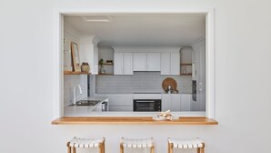 A compact kitchen with white cabinets, a wooden countertop, and a small dining area with two stools. - The Cape Retreat with stunning views (Cape Schanck)