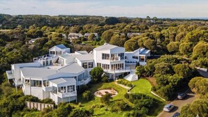 A modern, multi-story house with large windows, surrounded by lush greenery and a well-maintained lawn. - The Cape Retreat with stunning views (Cape Schanck)