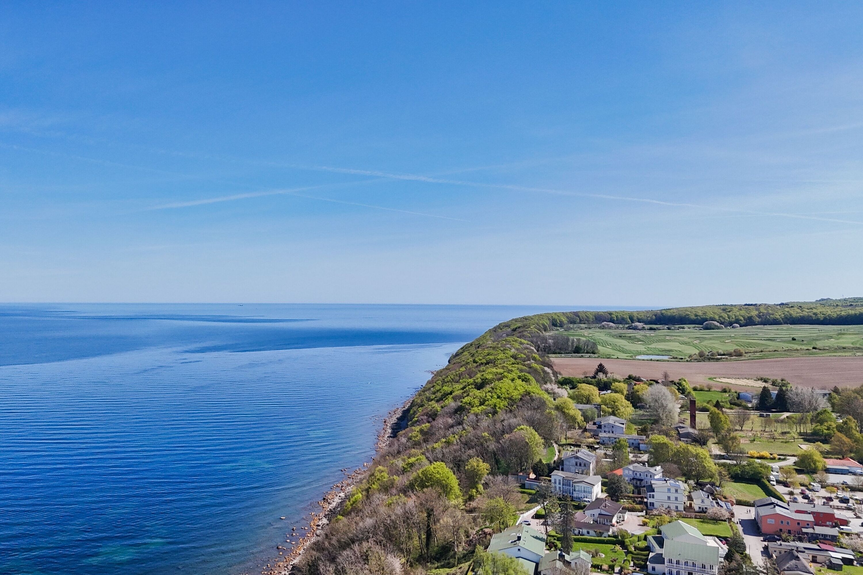 Eine Küstenwohngegend mit Häusern entlang der Uferlinie, wolkenlosem Himmel und Blick aufs Meer.