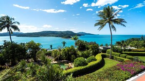 A tropical resort with a clear view of the ocean and mountains, well-maintained gardens, and a swimming pool.