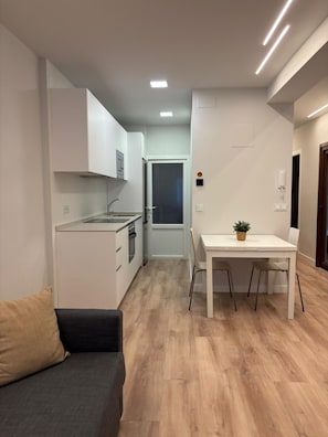 A compact kitchen with white cabinets, a dining table with chairs, and a small potted plant.