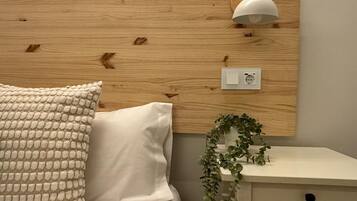 A bedroom with a wooden headboard, a bedside lamp, a white bedside table with a plant, and a textured pillow.