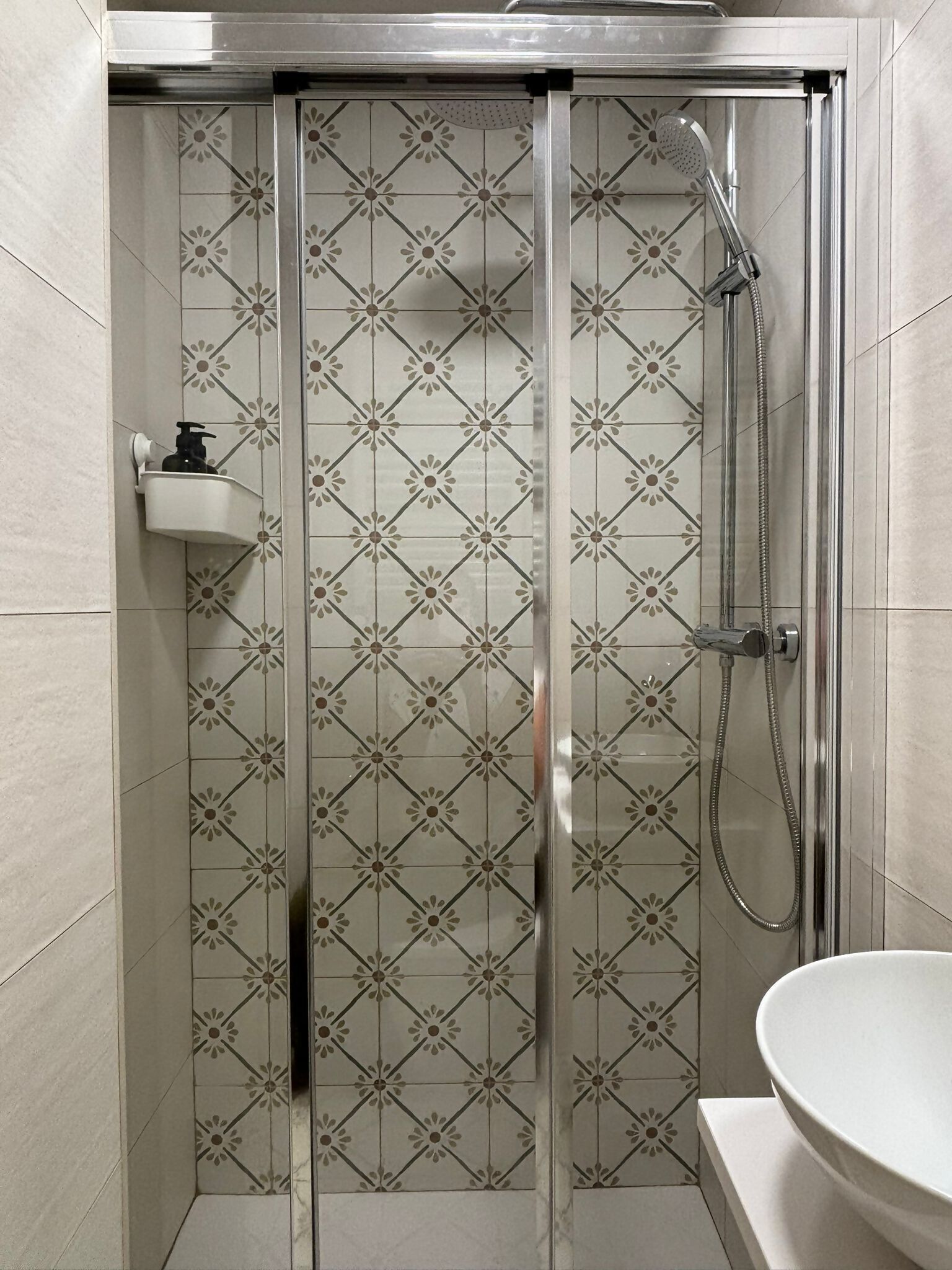 A shower with a glass door, a sink, and a patterned tile wall.