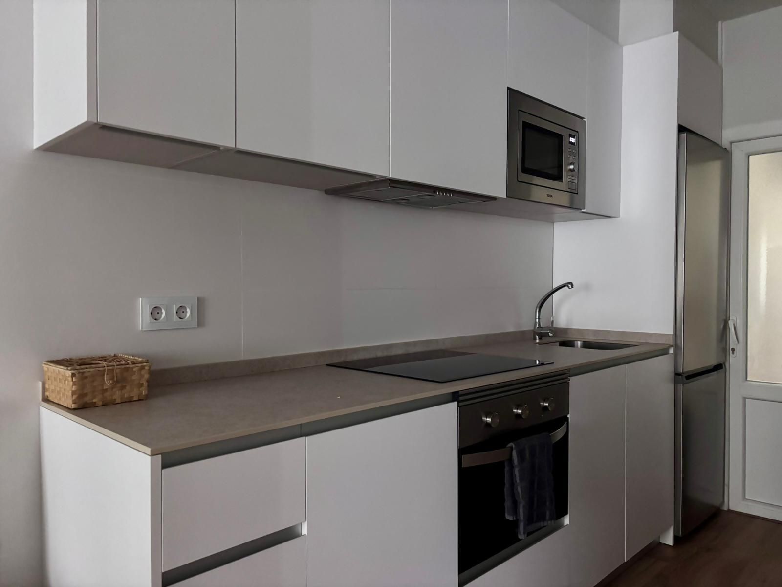 Een moderne keuken met witte kastjes, een ingebouwde magnetron, een roestvrijstalen spoelbak en een dubbele oven.