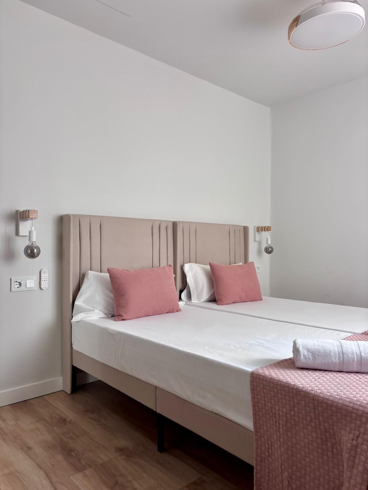 Una cama individual con cabecera, dos lámparas de noche, una mesita de noche y un enchufe en la pared.