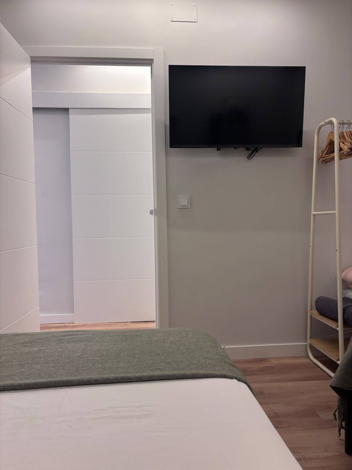 Un dormitorio con cama, televisión montada en la pared y armario.