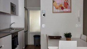 Et moderne køkken med hvide skabe, indbygget mikrobølgeovn og et spiseområde med et hvidt bord og stole.