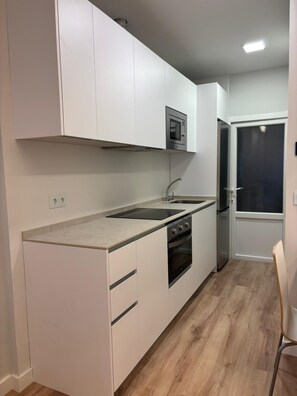 A modern kitchen with white cabinets, a stainless steel oven, a microwave, and a sink.