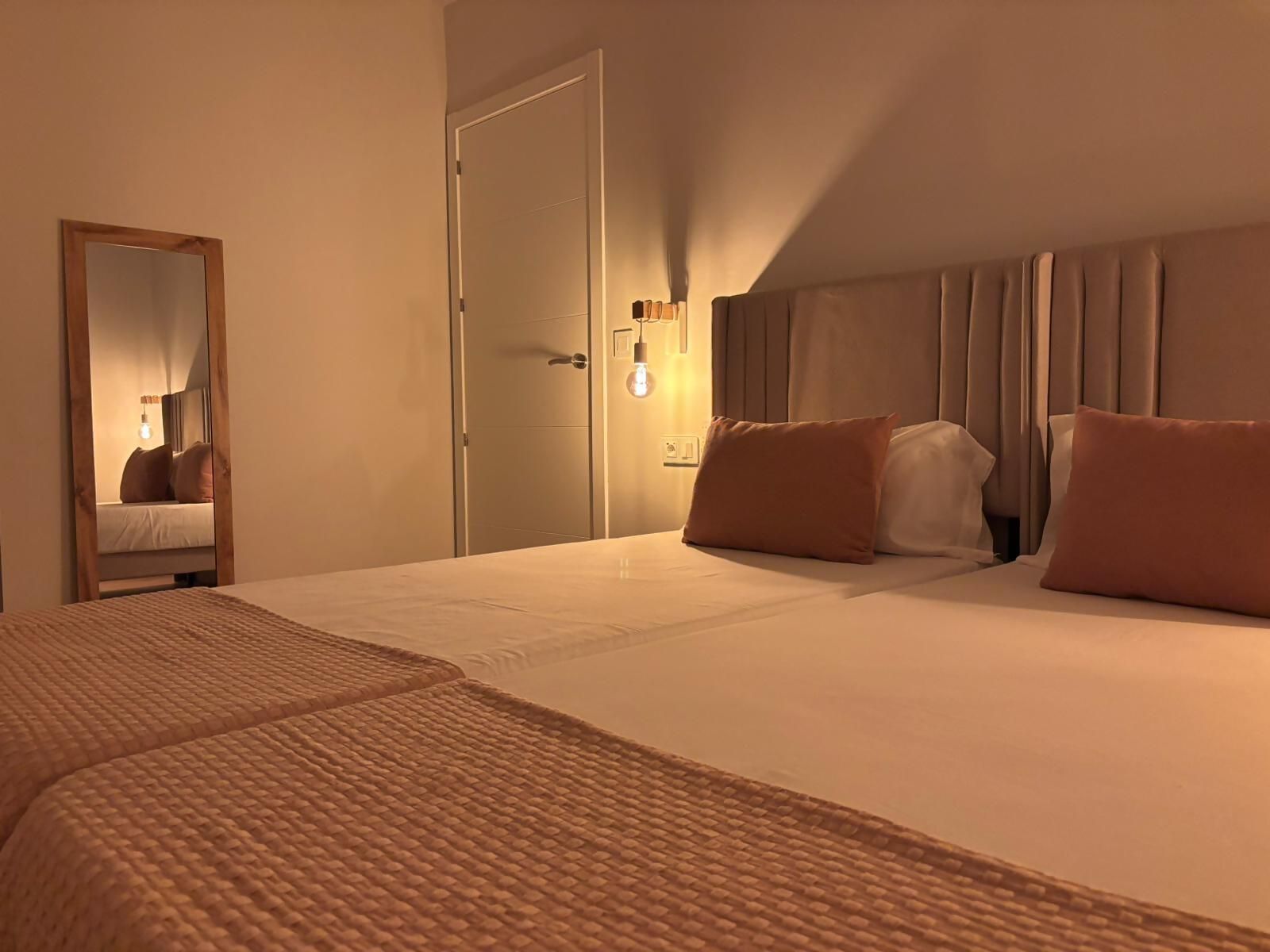 Habitación de hotel con una cama grande, un espejo, una puerta y una lámpara fijada a la pared.