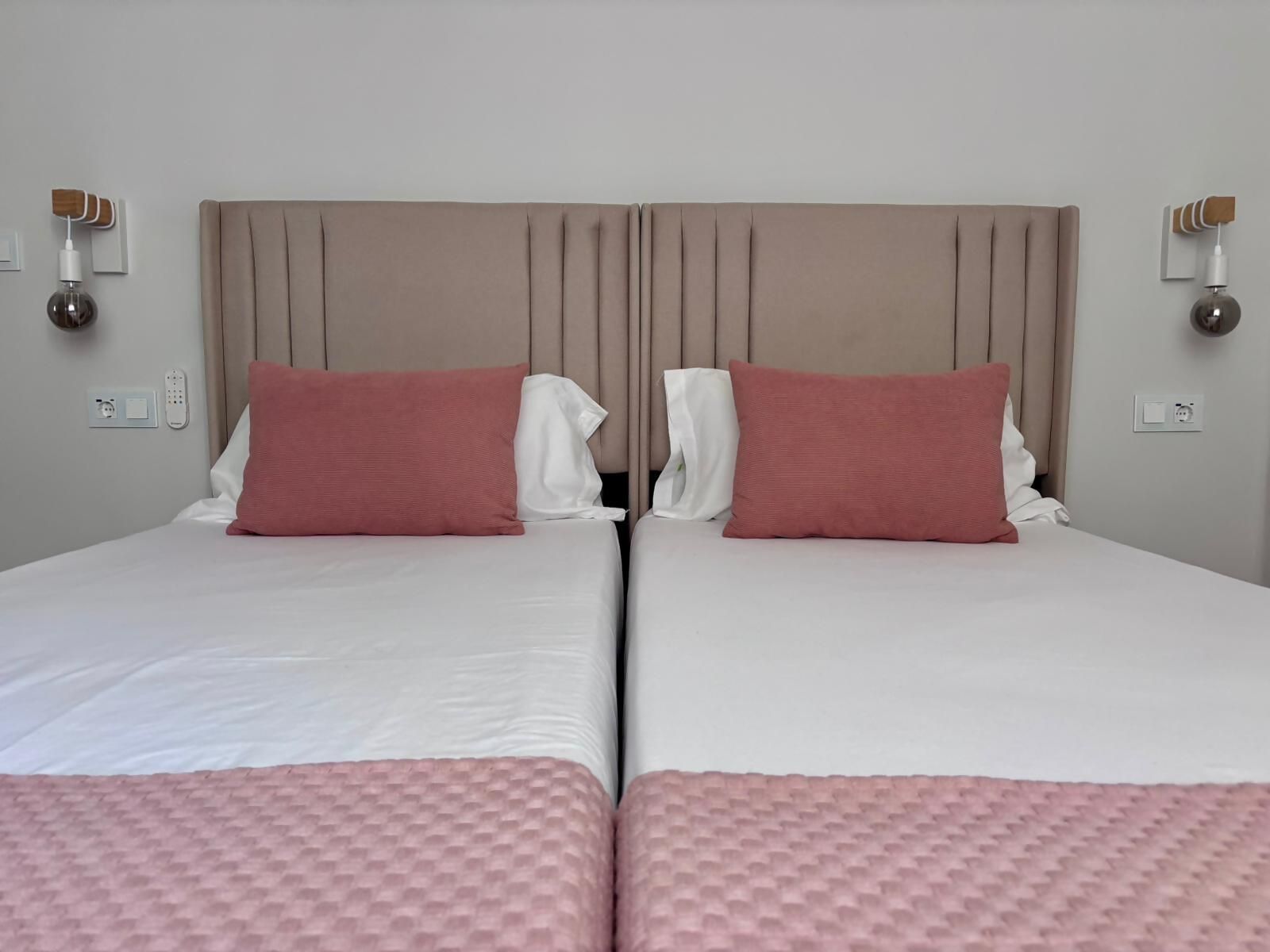 Cama doble con cabecera, dos almohadas, una mesita de noche y un enchufe de pared.