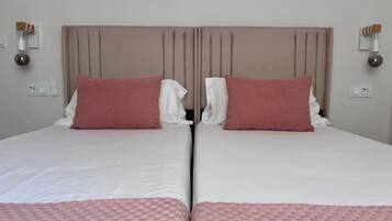 Cama doble con cabecera, dos almohadas, una mesita de noche y un enchufe de pared.