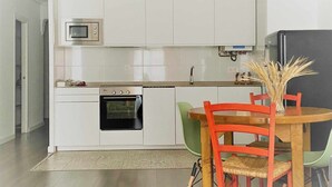 A modern kitchen with white cabinets, a built-in oven, a microwave, and a dining area with a wooden table and red chairs. - Apartamento en el Casco Antiguo de Pamplona - Ayla Camino de Santiago (Pamplona/Iruña)