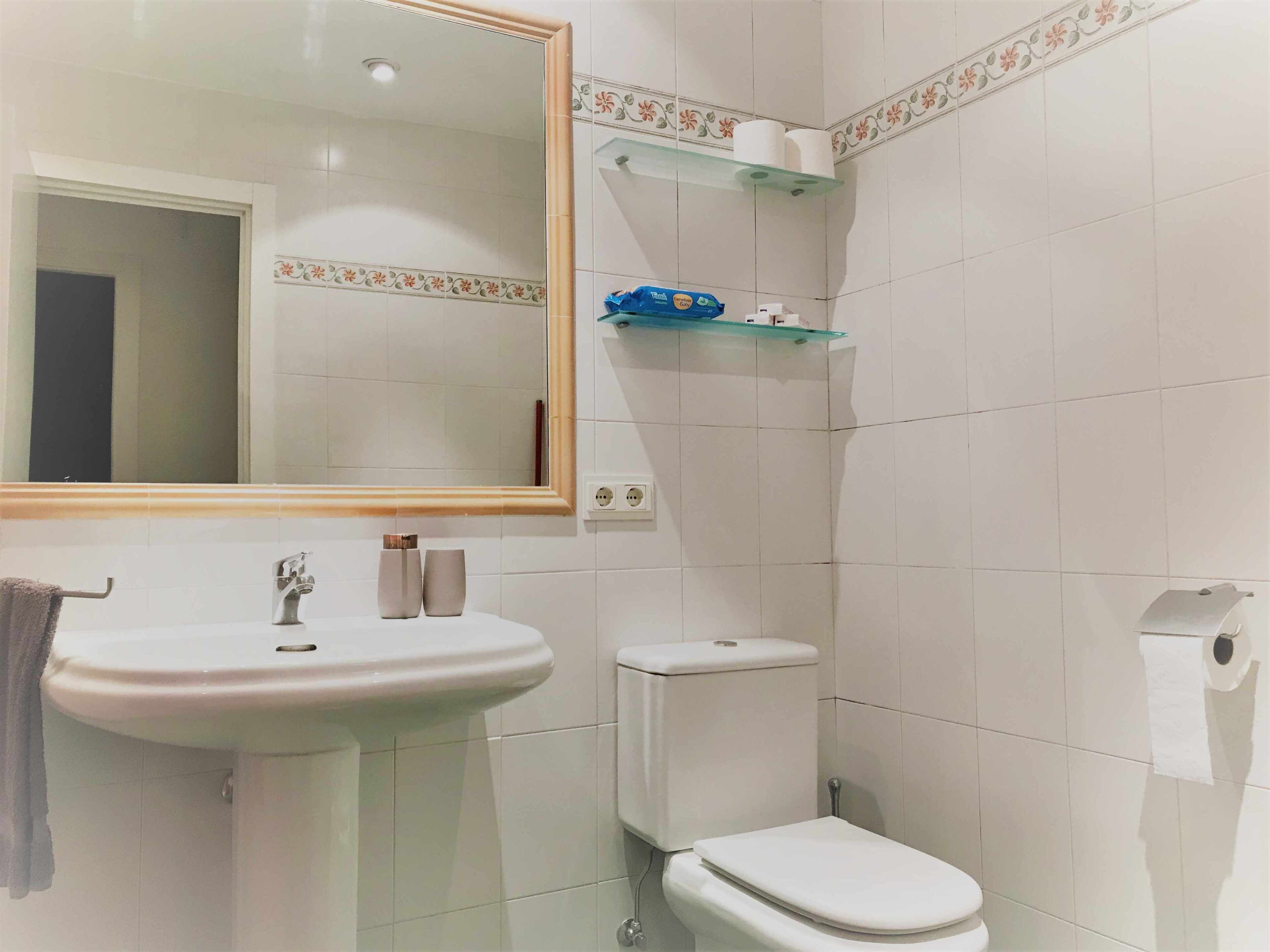 A bathroom with a sink, toilet, and mirror. There are shelves with toiletries and a towel hanging on the wall.