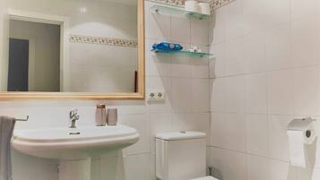 A bathroom with a sink, toilet, and mirror. There are shelves with toiletries and a towel hanging on the wall.