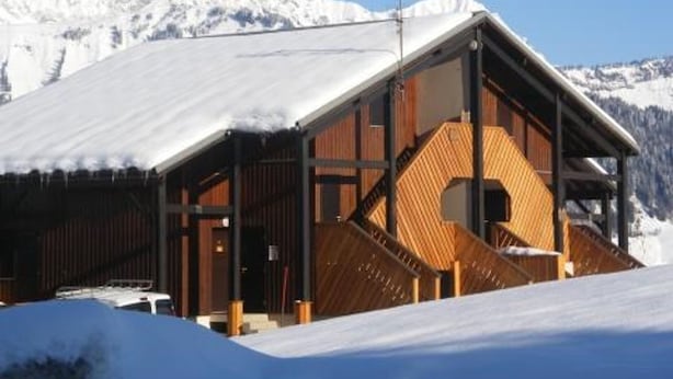 Une cabane en bois avec un toit en pente, de grandes fenêtres et un escalier en bois menant à l’entrée.