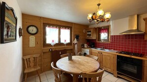 A cozy kitchen with wooden cabinets, a round wooden table with chairs, a stove, and a window with curtains. - Spacious 3-Bed Apt for 8, 80m from Cernix Slopes, Pet-Friendly, Terrace, Parking (Crest-Voland)
