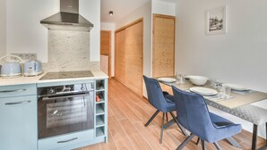 Una cocina moderna con horno empotrado, campana extractora de acero inoxidable y comedor con mesa para dos.