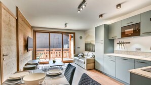 Una cocina moderna con armarios grises, un comedor con mesa dispuesta para cuatro personas y un balcón con barandillas de madera.