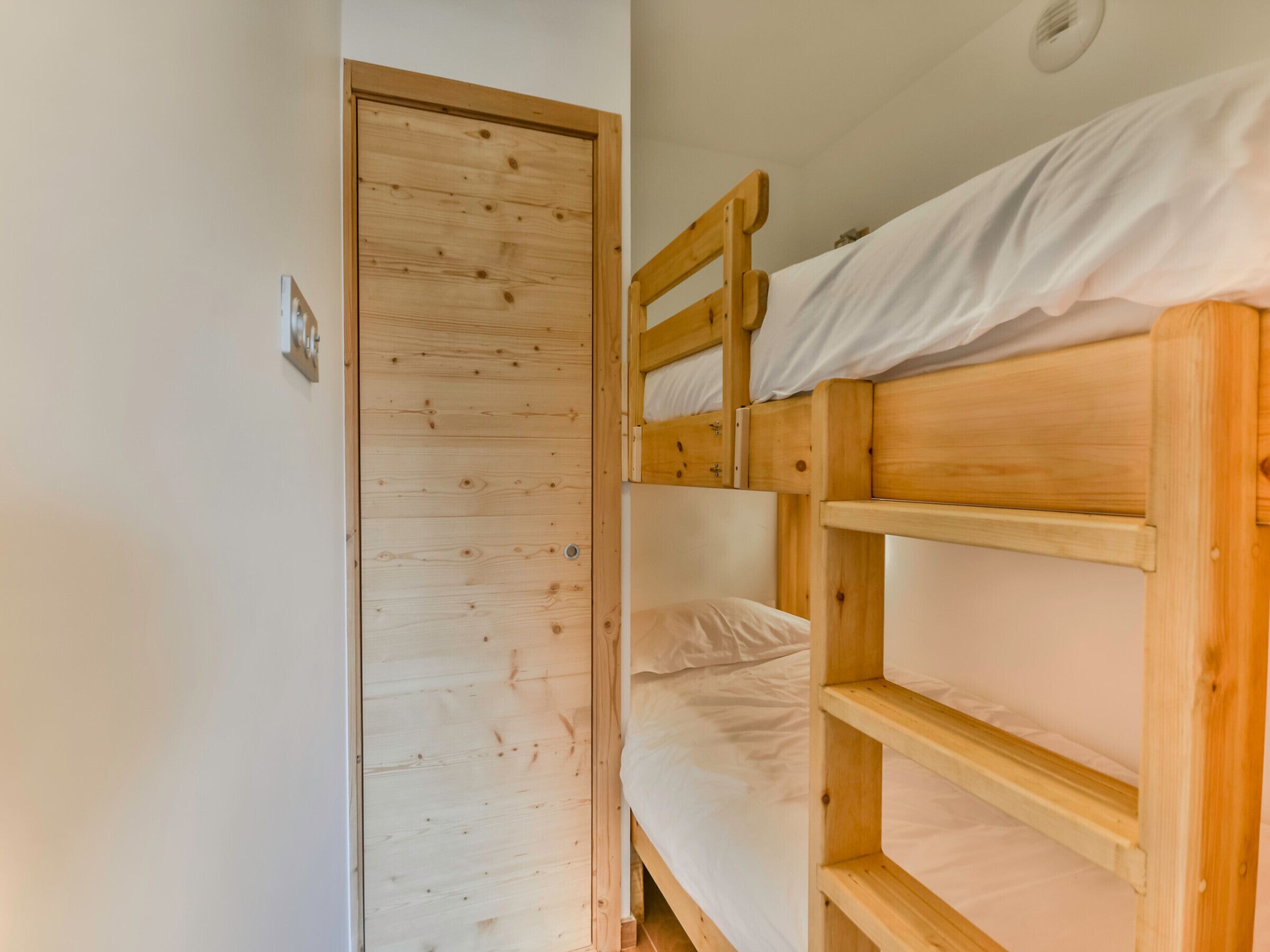 Quarto com beliche, porta de madeira e parede branca.