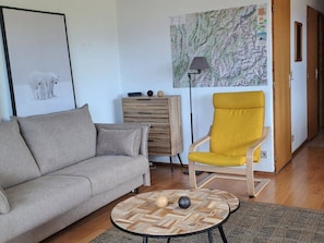 Una sala de estar con un sofá gris, un sillón amarillo, una mesa de centro de madera, un mapa en la pared y un mueble pequeño.