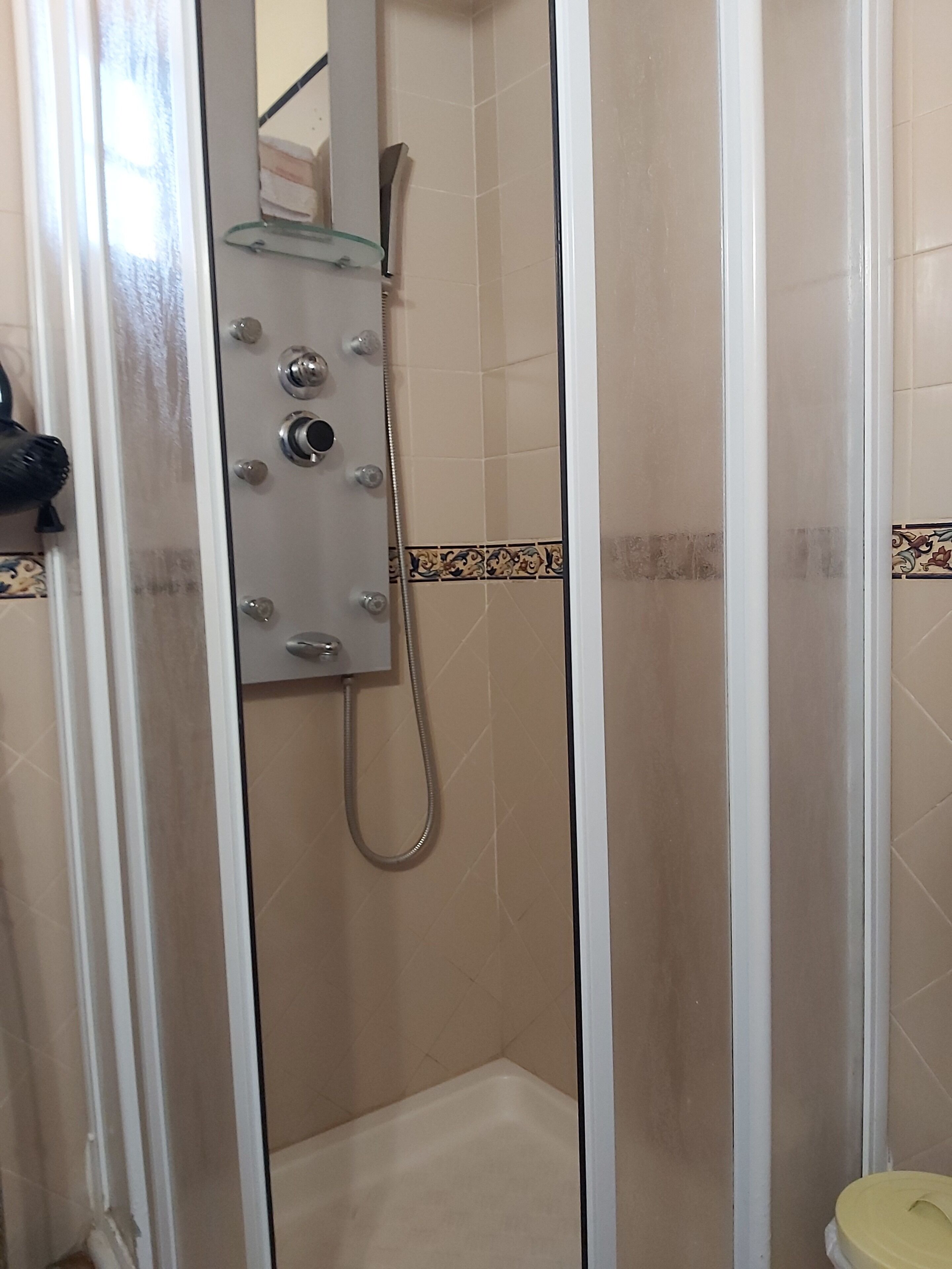 A shower enclosure with a glass door, a handheld showerhead, and a towel rack.