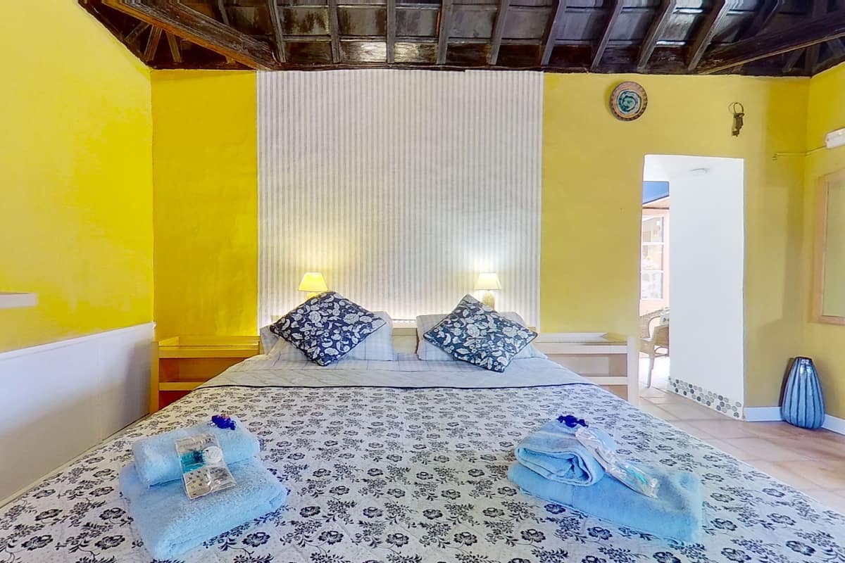 A hotel room with a bed, two bedside tables with lamps, a window, and a door leading to another room.