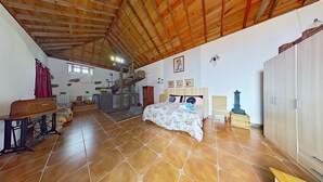 Una habitación amplia con techo de madera alto, una cama con ropa de cama floral, un escritorio de madera y una silla.