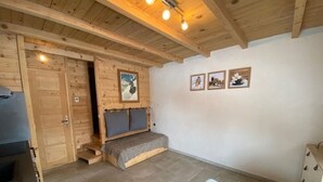 A cozy room with a wooden ceiling, a bed with a headboard, a small bench, and a dining area with chairs.