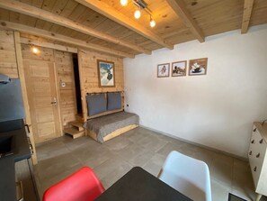 Quarto aconchegante com teto de madeira, cama com cabeceira, um pequeno banco e um espaço de refeições com cadeiras.
