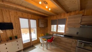 A wooden cabin-style kitchen with a dining table, chairs, and a refrigerator.