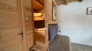 A wooden room with a bunk bed, a small staircase, and a single bed with a blanket.