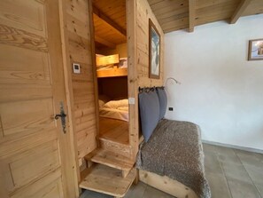 Quarto de madeira com beliche, um pequeno lance de escadas e uma cama de solteiro com cobertor.