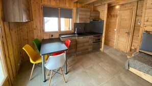A compact kitchen with wooden walls, a dining table with chairs, and a built-in oven.
