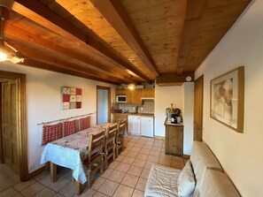 Cozinha acolhedora com vigas de madeira, área de refeições com mesa e cadeiras, e uma pequena cozinha compacta.