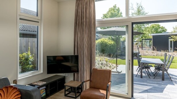 A modern living room with a flat-screen TV, a leather chair, and a dining area with a table and chairs. - Chalet with wide, deep backyard, sheltered and situated on the southwest<br>Decorated in a contemporary (Burgh-Haamstede)