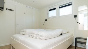 A single-bed room with a white bed, a small bedside table, a mirror, and a window with blinds. - Chalet with wide, deep backyard, sheltered and situated on the southwest<br>Decorated in a contemporary (Burgh-Haamstede)