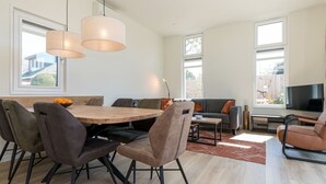 A modern living room with a dining area, large windows, and a flat-screen TV. - Chalet with wide, deep backyard, sheltered and situated on the southwest<br>Decorated in a contemporary (Burgh-Haamstede)