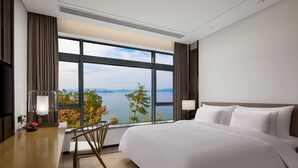 A hotel room with a large bed, a desk, and a view of the water. - Bright QiandaoLake Resort (Hangzhou)